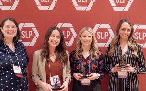 Four woman holding awards smiling in front of a red backdrop.